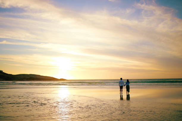 Small group of people walking along a tree-lined coastal path at sunrise